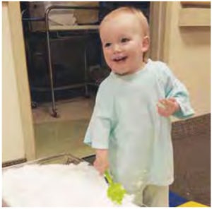 baby wearing hospital gown playing with a bin of snow