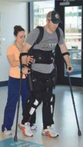 a man takes steps wearing the ReWalk exoskeleton with the assistance of a physical therapist