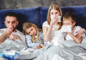 mom, dad, and kids snuggled up in bed with runny noses