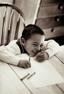 smiling child sitting at a table with paper and crayons