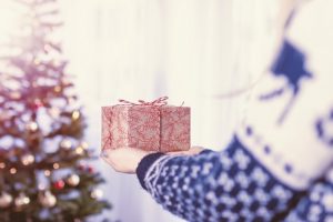 person holding out a wrapped gift, with Christmas tree in background