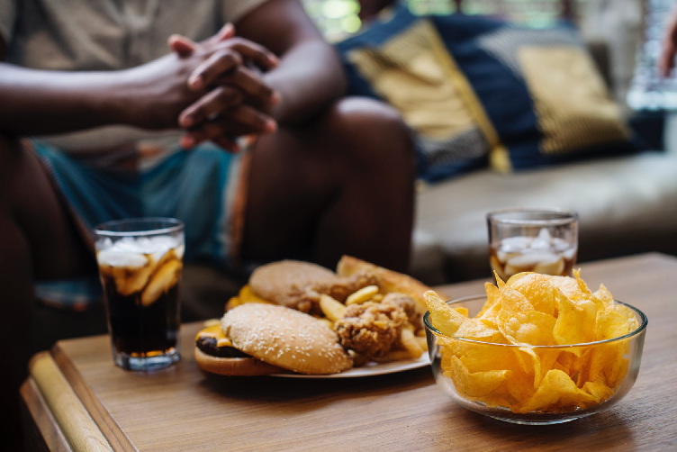 closeup of coffee table with sodas, chips, and fried foods on top