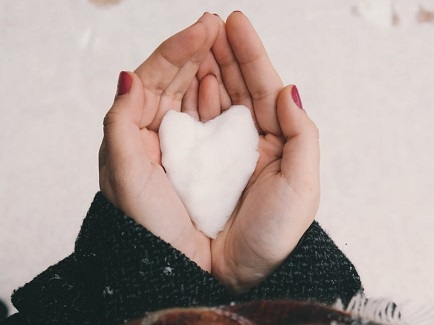 a person holding a heart-shaped piece of snow in their hands