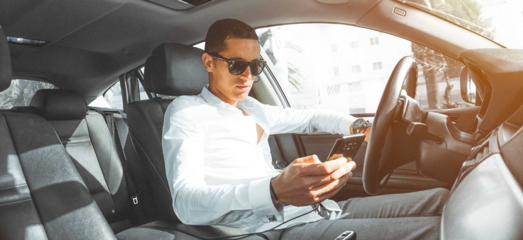 man looking at cell phone while sitting behind wheel of car