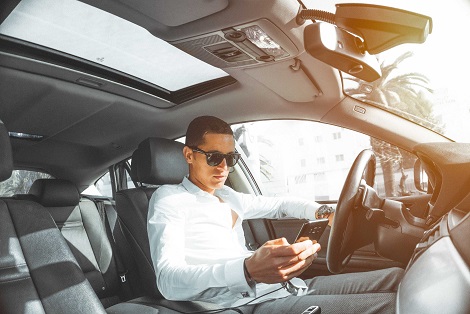 man looking at cell phone while sitting behind wheel of car