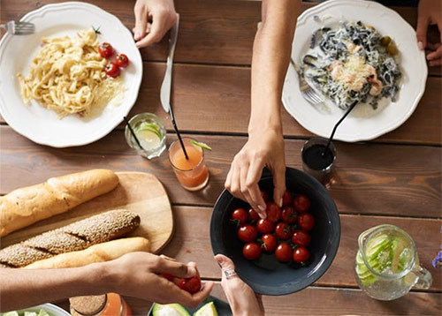 person taking a cherry tomato from a bowl on a communal lunch table