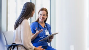 In the hospital waiting room, the mature adult female surgeon smiles as she gives the unrecognizable female family member good news.